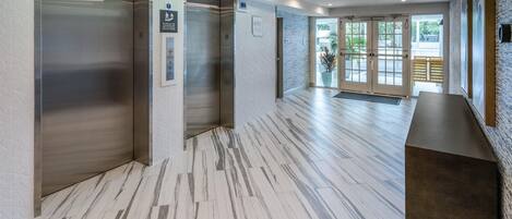 A modern lobby with a marble floor, elevators, and a reception desk.