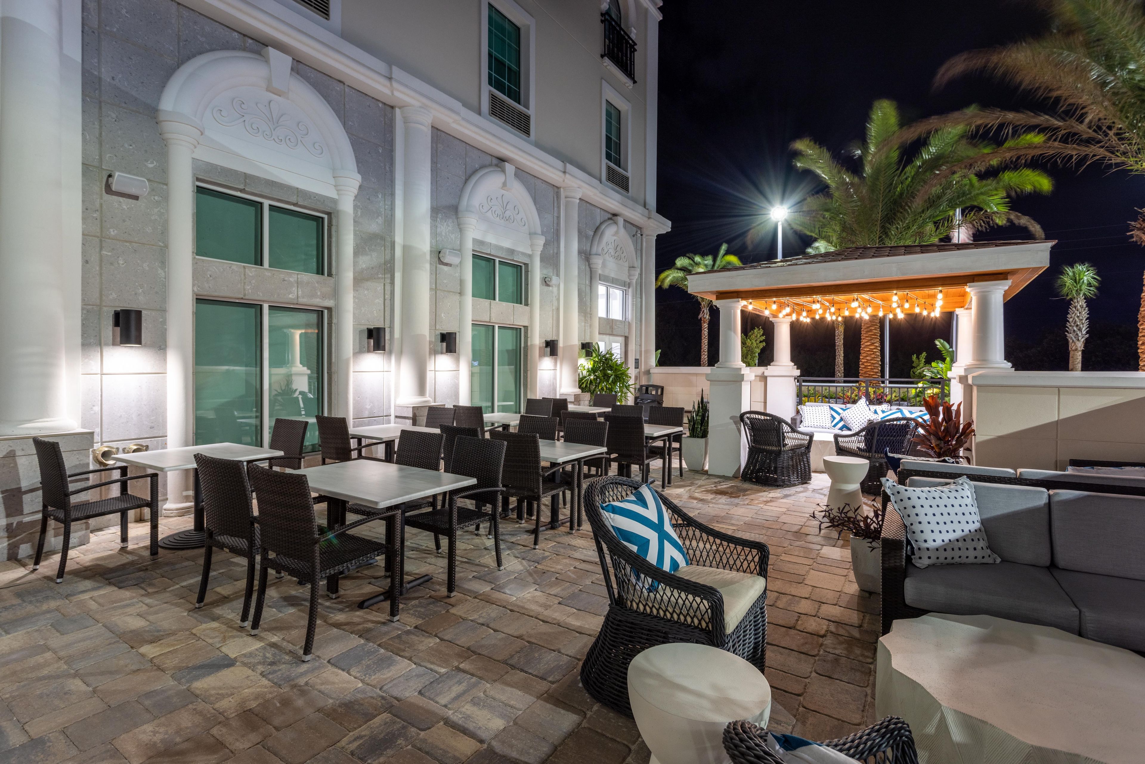 An outdoor patio area with tables and chairs, a seating area with a sofa, and a covered section with string lights.