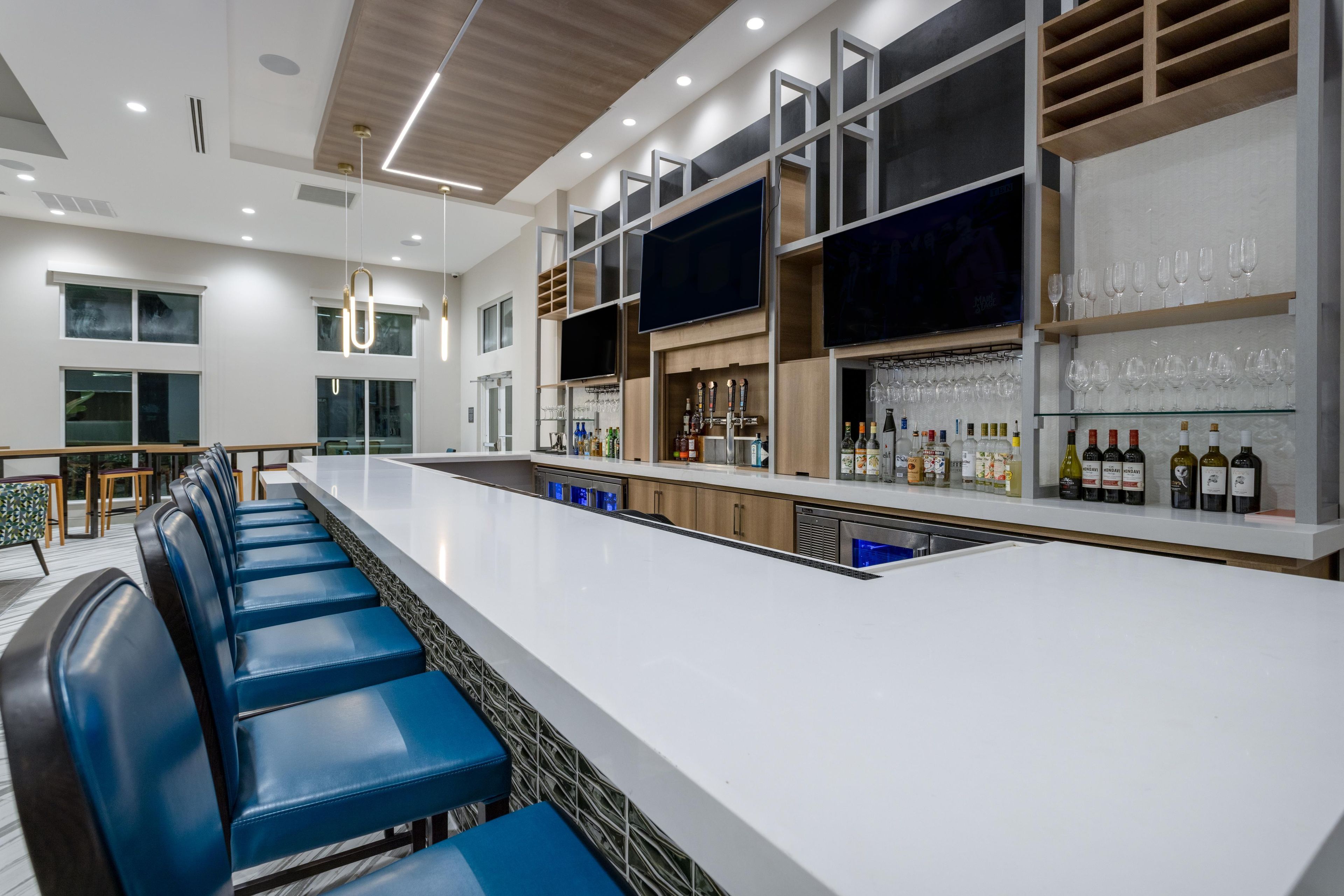 A modern bar area with a long counter, blue bar stools, and a wine display.