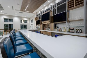 A modern bar area with a long counter, blue bar stools, and a wine display. - Hilton Garden Inn St. Augustine Historic District (St. Augustine)