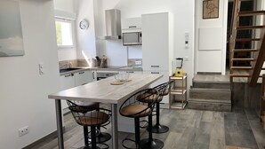 Ett modernt kök med en köksö i mitten, barstolar, en mikrovågsugn och en mixer på en hylla.