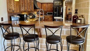 A kitchen with wooden cabinets, a central island with bar stools, and a refrigerator. - Walk to ski & trails! Luxury lodge, sleeps 17, hot tub, fire pit & fenced yard. (Angel Fire)
