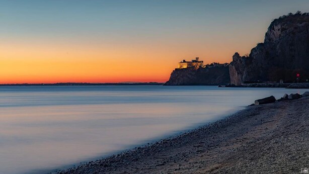 Un paysage côtier avec une falaise et un bâtiment au sommet, surplombant des eaux calmes.