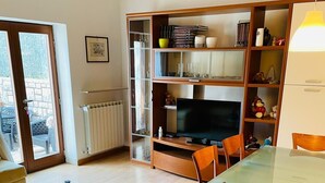 Un salon comprenant un canapé, une table basse en verre, une table à manger avec des chaises, un téléviseur et une bibliothèque.