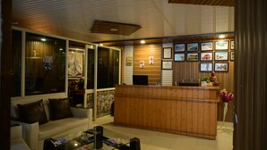 A reception area with a wooden desk, a sofa, and a glass coffee table. - Aanantham Country Resort (Chamba)