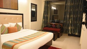 A hotel room with a large bed, a red rug, a sofa, and a window with curtains. - Aanantham Country Resort (Chamba)
