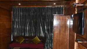 A wooden cabin interior with a bench, curtains, a television, and a fireplace. - Aanantham Country Resort (Chamba)