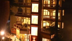 A multi-story building with balconies and windows illuminated at night. - Aanantham Country Resort (Chamba)