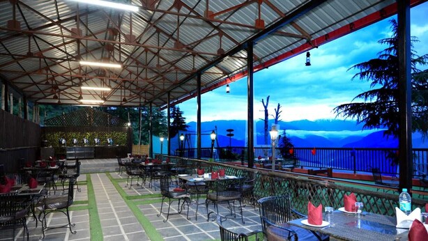 An outdoor restaurant with tables and chairs, a covered seating area, and a view of the mountains. - Aanantham Country Resort (Chamba)