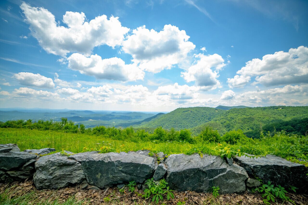 A scenic landscape with a stone wall in the foreground and a view of green hills under a blue sky with clouds.