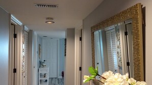 Un couloir avec un sol à motifs, une porte blanche au fond et un miroir décoratif accroché au mur.