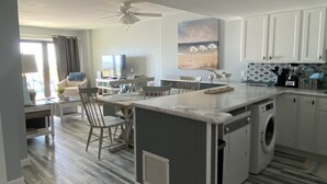 Une cuisine moderne avec un îlot central, un coin repas avec des chaises, un téléviseur et un tableau au mur.