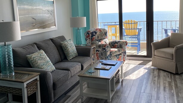 Un salon comprenant un canapé, une table basse et des fauteuils, un ventilateur de plafond, un tableau et une vue sur l’océan par une porte-fenêtre coulissante.