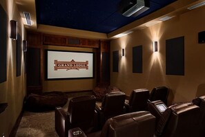 Ein Heimkinozimmer mit einer Leinwand, auf der 'GRAND LODGE' zu sehen ist, mit ledernen Liegesesseln und einer Sternenhimmel-Decke.