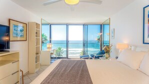 A hotel room with a bed, a desk, a television, a bookshelf, a chair, a lamp, and a view of the ocean. - Capri by the Sea 203 | Ocean View | Full Kitchen | Private Bedroom | Beach Access | On the Boardwalk (San Diego)