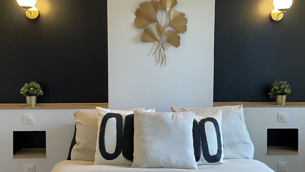 A modern bedroom with a large bed, two wall-mounted light fixtures, and a decorative wall piece. - L'Appartement Bleu - Cosy apartment - Heart of town (Douai)