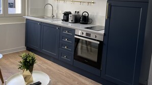 A modern kitchen with dark blue cabinets, a stainless steel range, and a built-in oven. There is a small round table with a plant and a remote control. - L'Appartement Bleu - Cosy apartment - Heart of town (Douai)