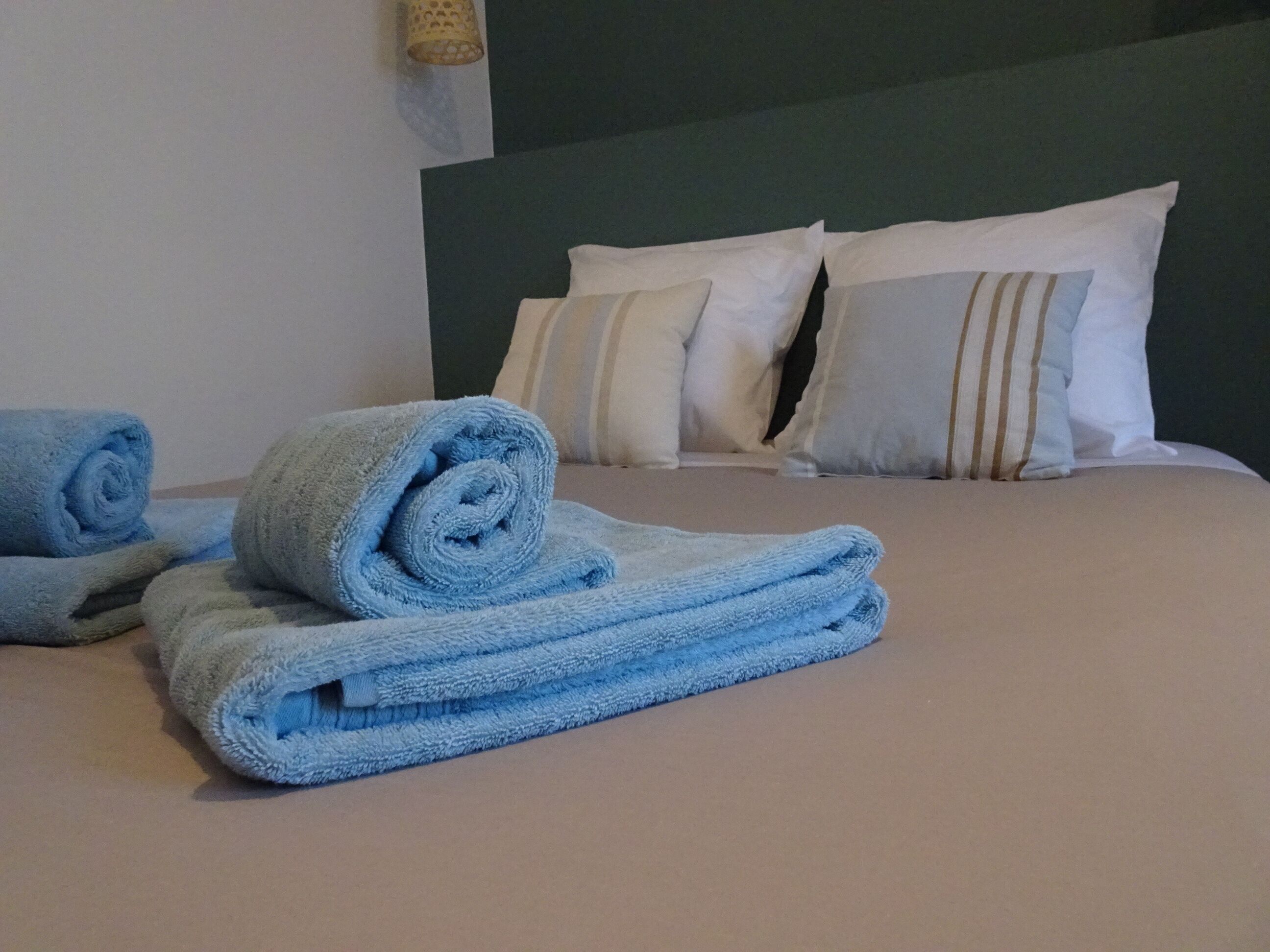 Un lit bien fait, avec des serviettes bleues, des oreillers blancs et une tête de lit verte.