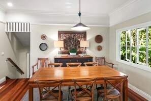 A dining area with a wooden table and chairs, a pendant light, and a window with a view of greenery.