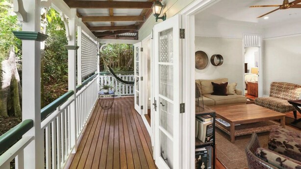 Eine überdachte Veranda mit Holzboden, weißen Geländern und Blick auf den Garten.