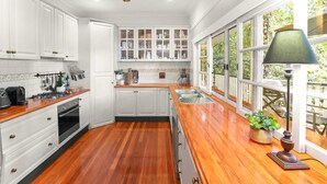 Eine Küche mit weißen Schränken, einer Holzauskleidung, einem eingebauten Backofen und einem großen Fenster mit Blick auf Grünflächen.