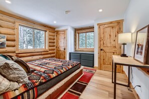 Een slaapkamer in een blokhut met een bed, twee ramen, een bureau en een dressoir.