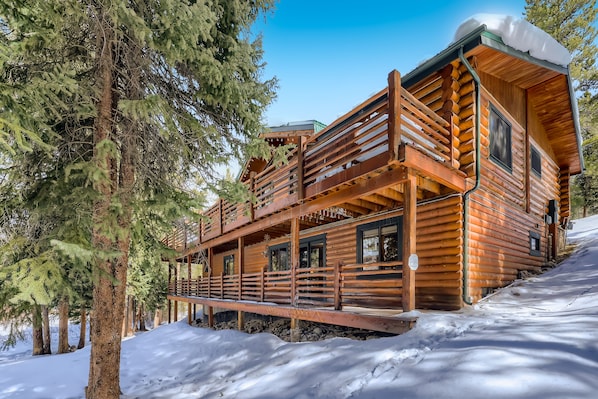 A log cabin with a balcony, surrounded by snow and trees.