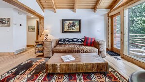 Una sala de estar acogedora con techo de madera, un sofá de cuero marrón, una mesa de centro y un ventanal con vistas al exterior.
