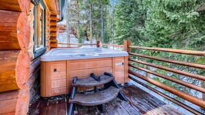Una cabaña de madera con jacuzzi en una terraza, rodeada de árboles.