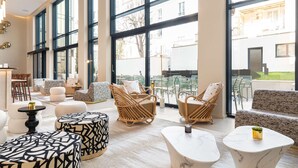 A spacious lounge area with large windows, wicker furniture, and a marble coffee table. - Hotel Yac Paris Clichy, A Member Of Radisson Individuals (Clichy)