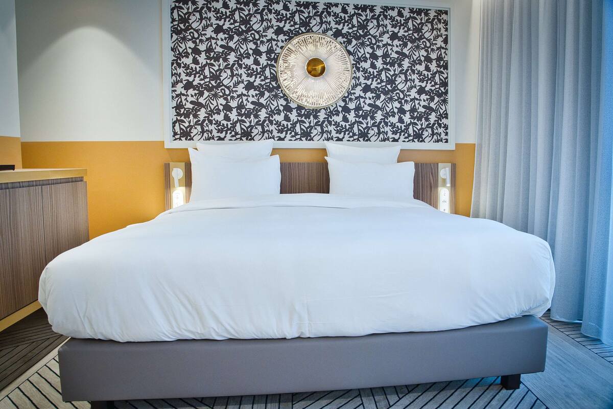 A large bed with white linens, a wall-mounted decorative piece, and a wooden headboard.