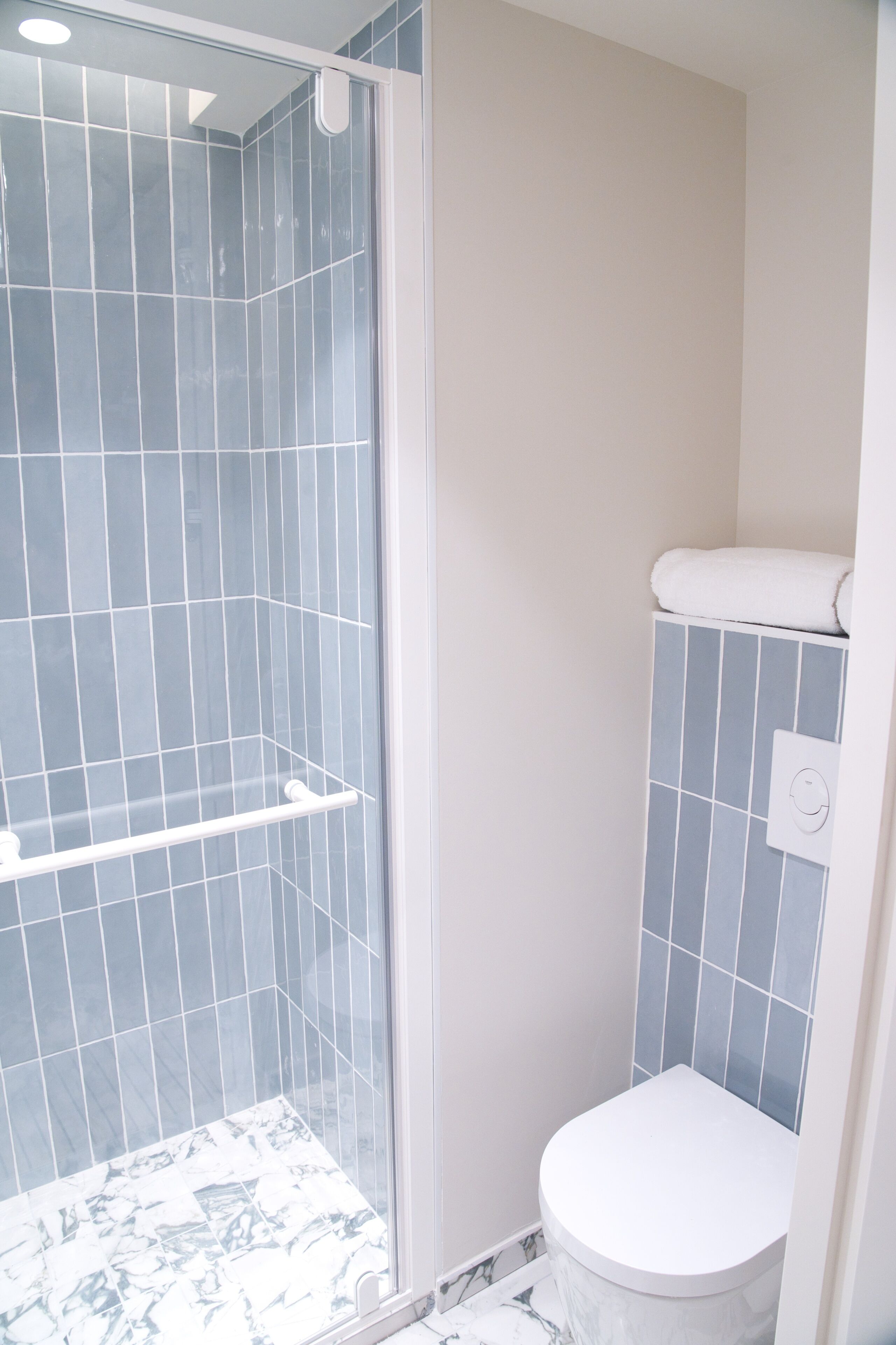 Een badkamer met een douche met glazen wand, een toilet en een vloer met marmerpatroon.