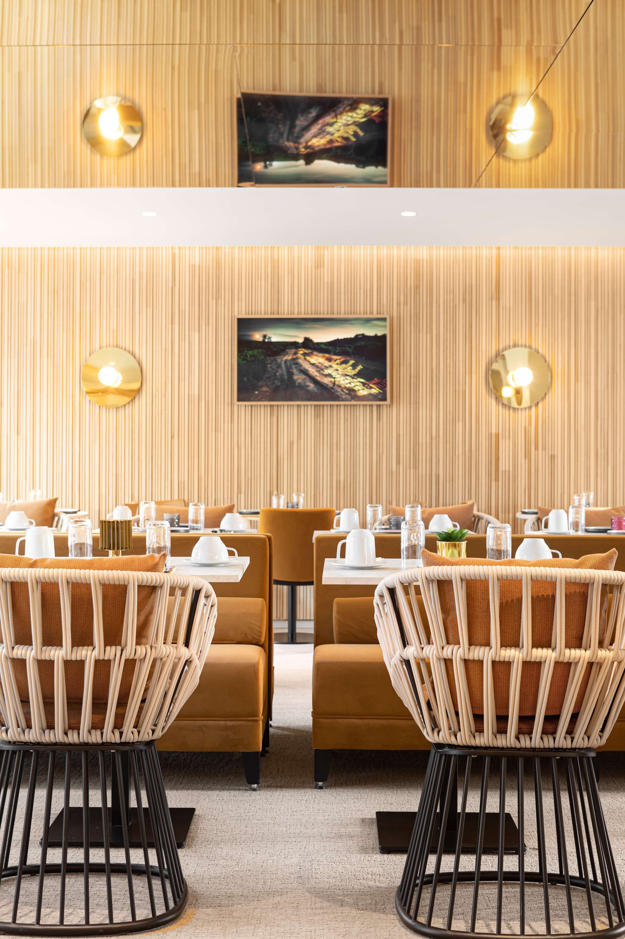 A restaurant with a warm wooden wall, two framed pictures, and a table set with white plates and glasses.