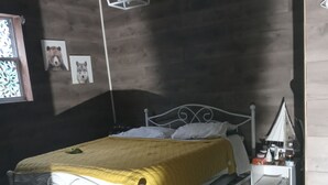 Ein Schlafzimmer mit Bett, Nachttisch, kleinem Tisch, einer Pendelleuchte und einem Fenster mit dekorativem Blick.