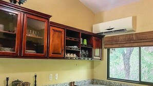 A kitchen with wooden cabinets, a granite countertop, and a window with a view of trees. - Tropical Hideaway 2+2 Condo in Playa Coco Guanacaste (Ocotal, Sardinal, Carrillo)
