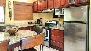 A kitchen with wooden cabinets, a microwave, a stove, and a refrigerator. - Tropical Hideaway 2+2 Condo in Playa Coco Guanacaste (Ocotal, Sardinal, Carrillo)