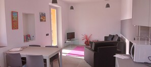A modern living space with a dining area, a sofa, a TV, and a kitchen area.