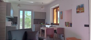 A modern kitchen with a dining area, large windows, and a view of greenery.