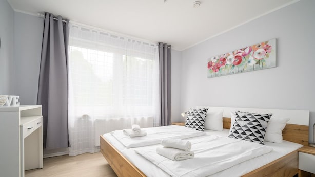 A modern bedroom with a wooden bed, white bedding, and a painting of flowers on the wall. - Vacation apartment Mila am Schwarzer See - Lake District (Schwarz)