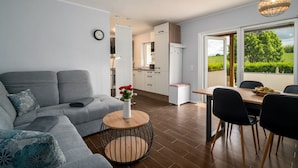 A modern living room with a grey sofa, a round wooden coffee table, and a dining area with a wooden table and black chairs. - Vacation apartment Mila am Schwarzer See - Lake District (Schwarz)