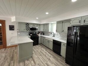 A modern kitchen with white cabinets, a black refrigerator, stainless steel appliances, and a wooden floor. - Spacious Vacation home in Chimney Hill near Mt Snow (Wilmington)