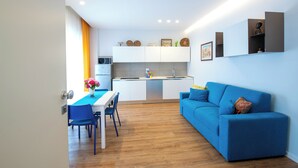 A modern kitchen with white cabinets, a dining area with blue chairs, and a blue sofa.