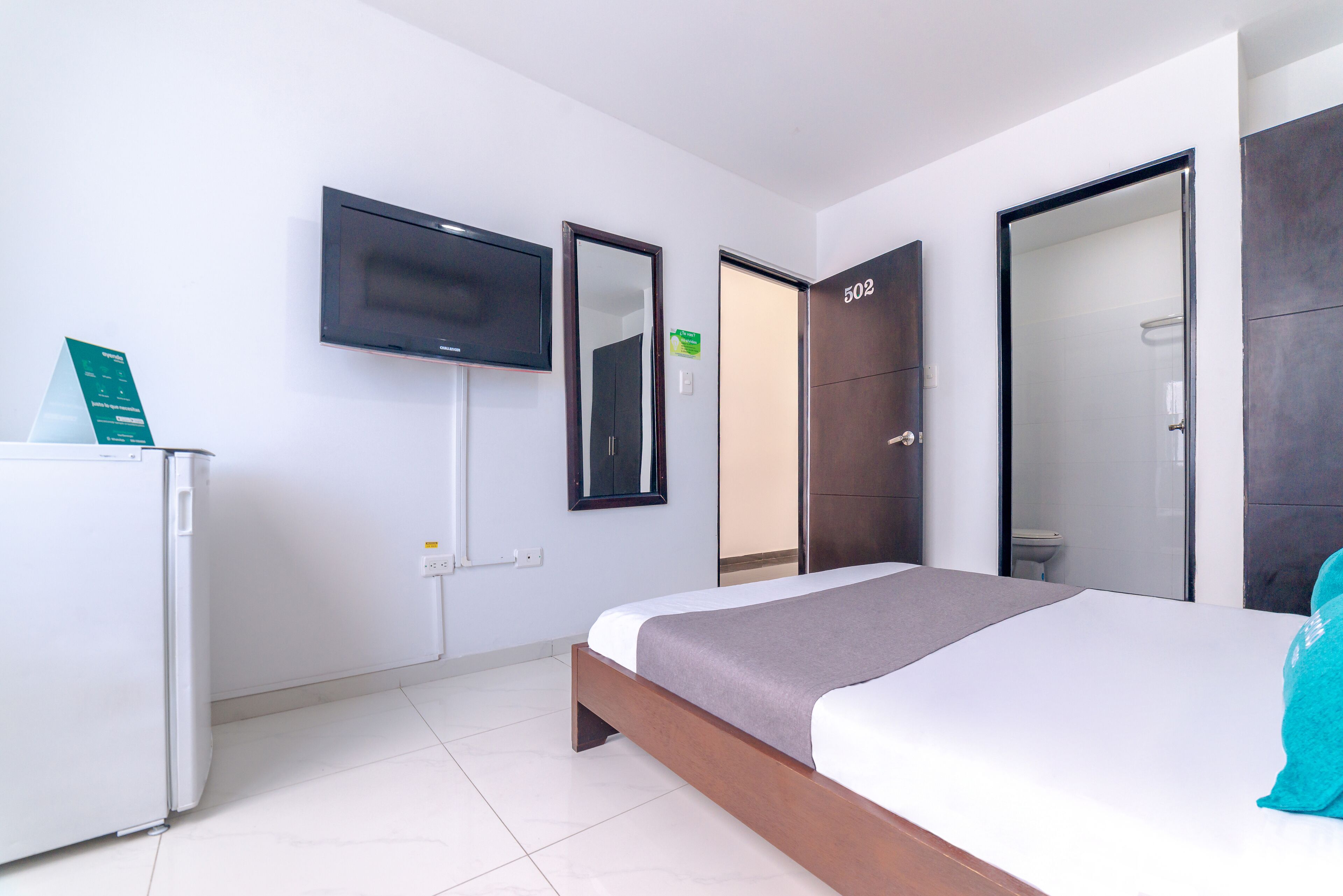 Habitación de hotel moderna con una cama, televisión, armario y baño visible a través de una puerta.