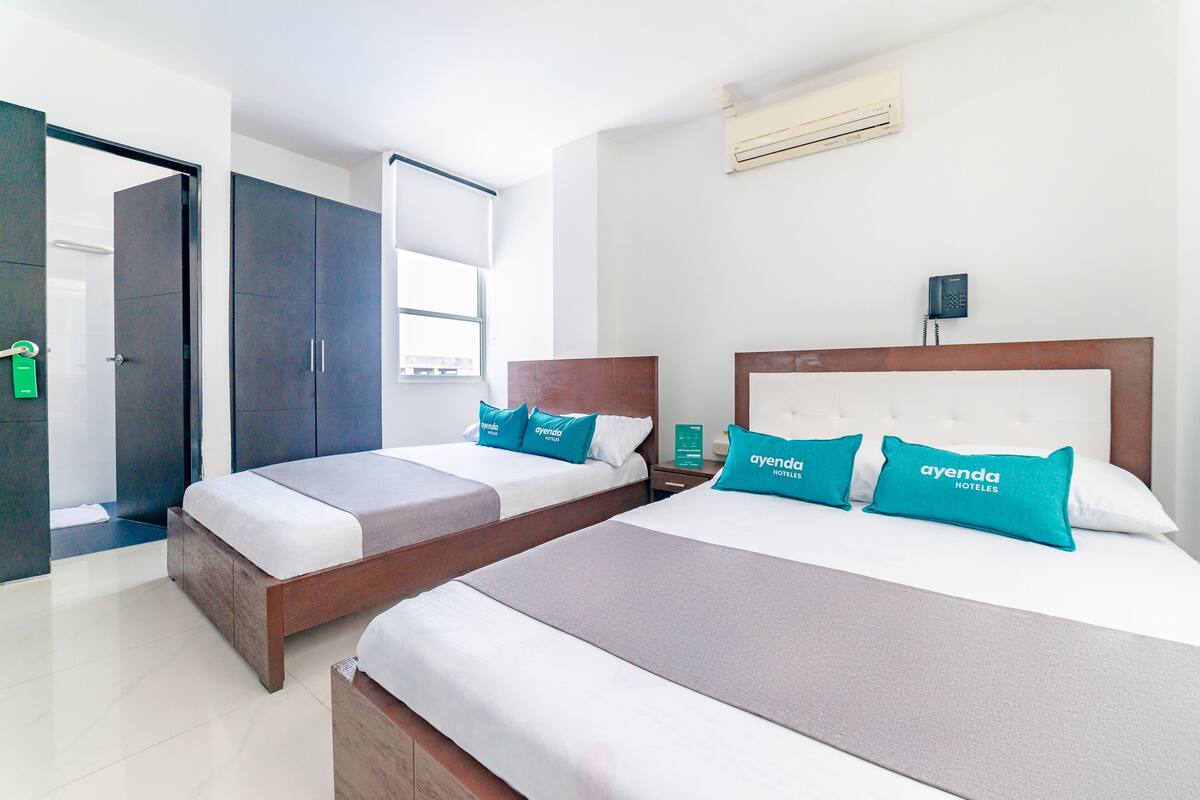 Quarto de hotel com duas camas, um guarda-roupa, uma mesa de cabeceira, um ar condicionado e um telefone.