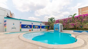 Una piscina con solárium de azulejos, un mural en la pared y una palmera al fondo.