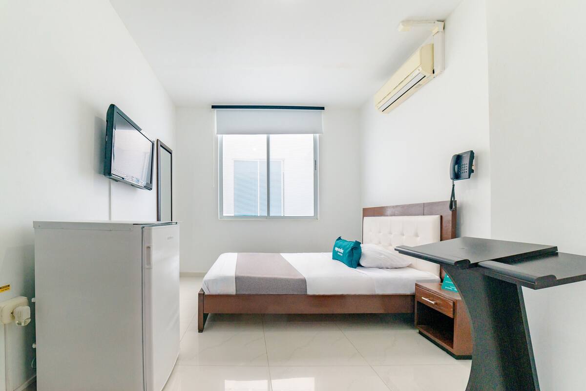 Quarto de hotel com cama, escrivaninha, televisão, telefone e janela.
