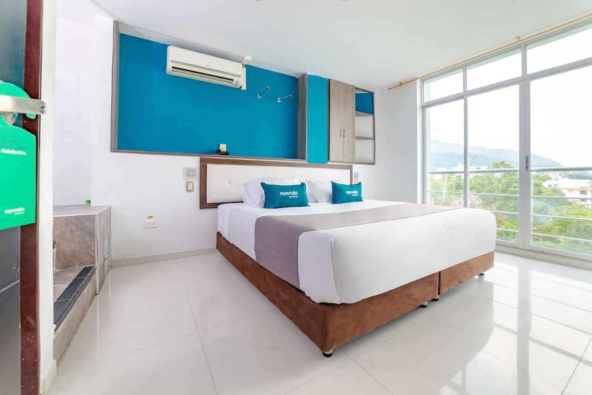 Quarto de hotel moderno com cama grande, guarda-roupa embutido, grande janela com vista para a cidade e ar condicionado na parede.
