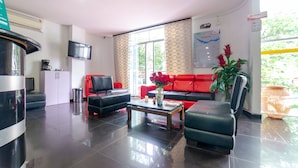 Un moderno vestíbulo de hotel con un sofá de cuero negro, un sofá rojo, una mesa de centro de vidrio y una gran planta en maceta.