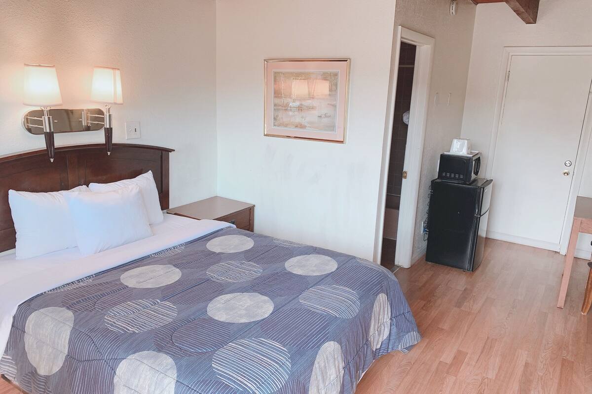 A neatly arranged bedroom with a bed, bedside lamps, a framed picture on the wall, and a small cabinet with a microwave.