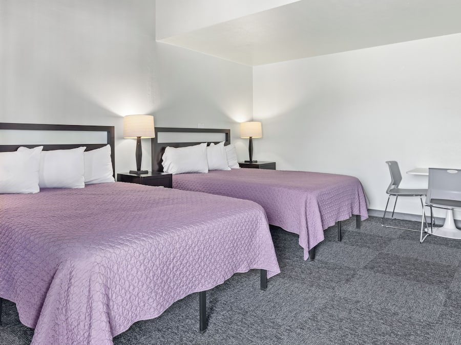 A hotel room with two beds, nightstands with lamps, a desk, and a chair.